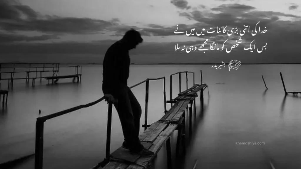 Very Sad Poetry with a black and white cinematic shot of a lonely man standing on a wooden pier over a calm lake at dusk. The background shows a vast, cloudy sky. White Urdu calligraphy is overlaid on the right side, featuring a soulful couplet by Bashir Badr about loss and longing.